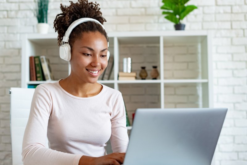 Portrait of a happy mulatto woman freelancer working on laptop in earphones and listening to music