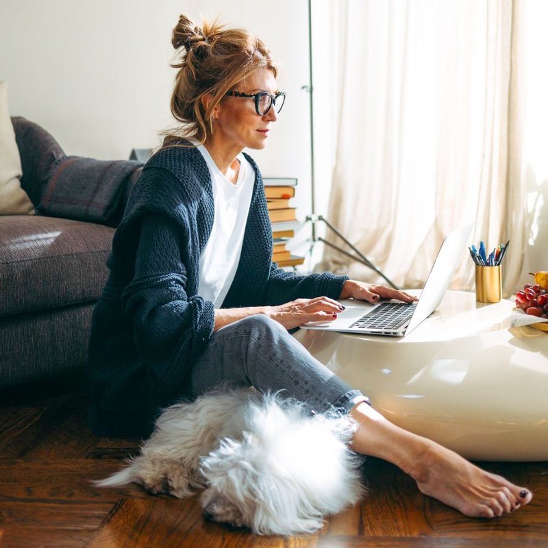 A woman focused and working on her laptop with her dog napping by her side