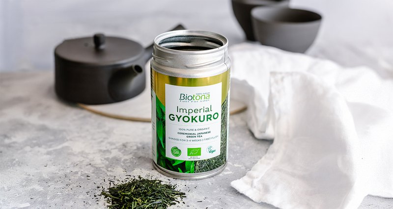 Biotona Imperial Gyokuro blikje met theepot en kopje op de achtergrond en losse thee op de voorgrond.