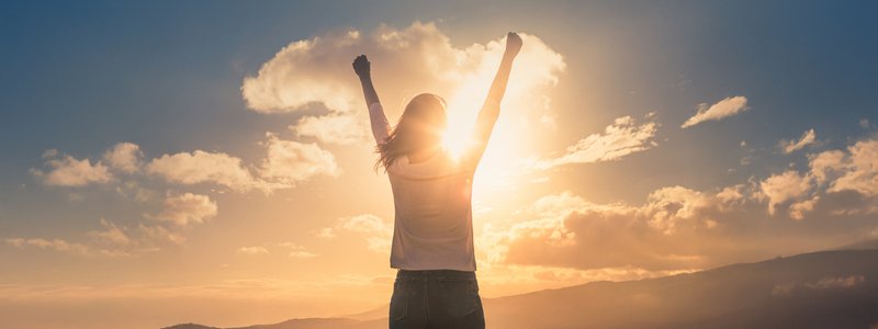 Vrouw met armen in de lucht, kijkend naar bergen en zon, uitstralend energie en vrijheid tijdens menopauze