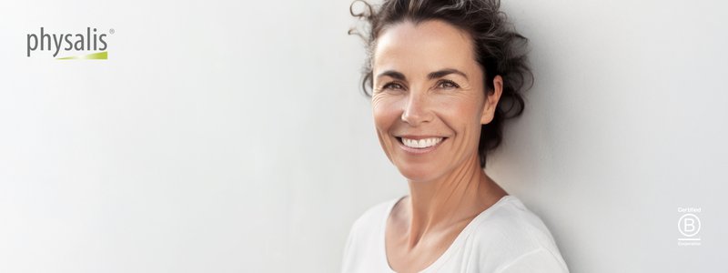 Lachende rijpere vrouw in witte top, straalt gezondheid en welzijn uit tijdens perimenopauze