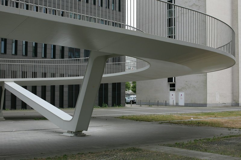 A curved white concrete staircase on the exterior of a minimal building, photographed from below against a pale sky, architectural and understated.