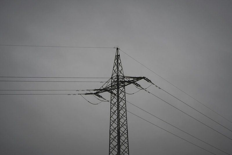 A black electric utility pole and power lines against a uniform gray sky, minimal and monochromatic, high negative space above the lines.