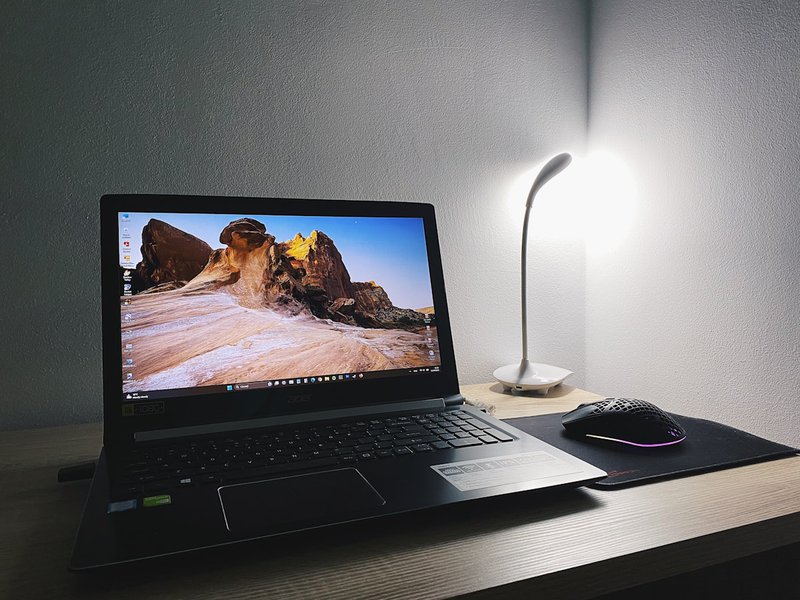 A laptop computer sitting on a wooden desk surface, warm natural light, the quiet presence of a tool waiting to be used for something specific