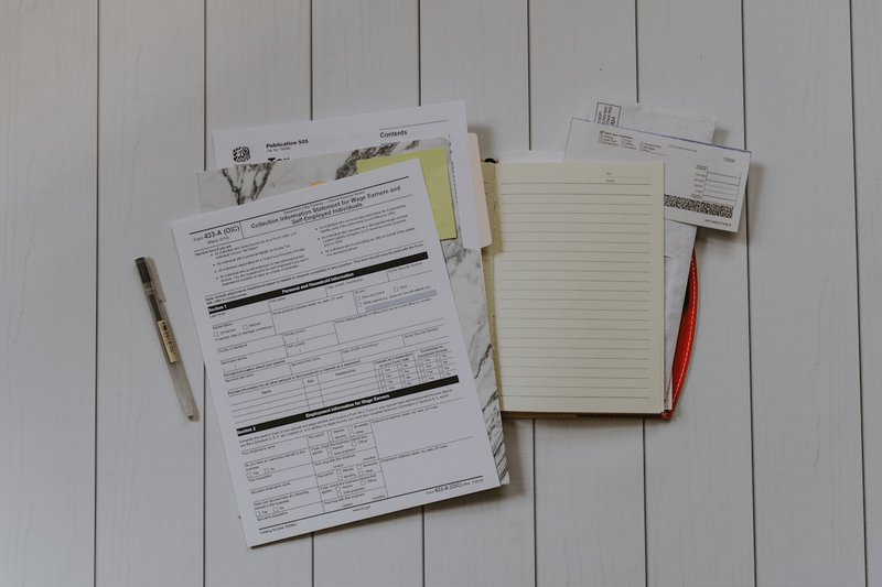 A stack of papers photographed from directly above in flat lay, the overhead mechanical arrangement of accumulated paperwork, the visual weight of obligations left unattended