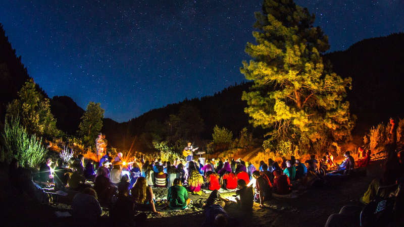 An audience gathered outdoors to listen to a man playing a guitar.