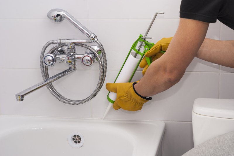 Reglazing for contractors. Man applying caulk on bathtub surface.