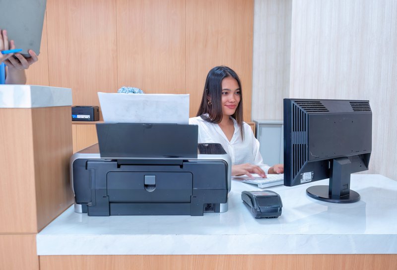 a printer on the desk and a worker smiling while working on the computer