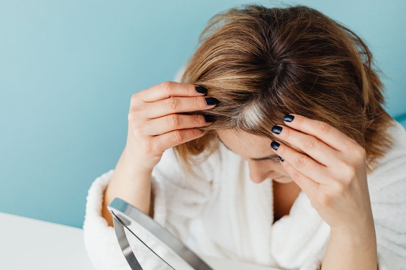 A woman examining hair roots and scalp conditions.