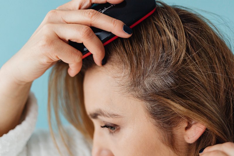 A woman combing her hair, a regular practice for maintaining scalp health.