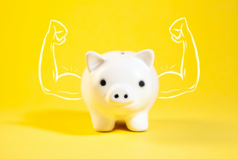 A white piggy bank with drawn muscular arms.