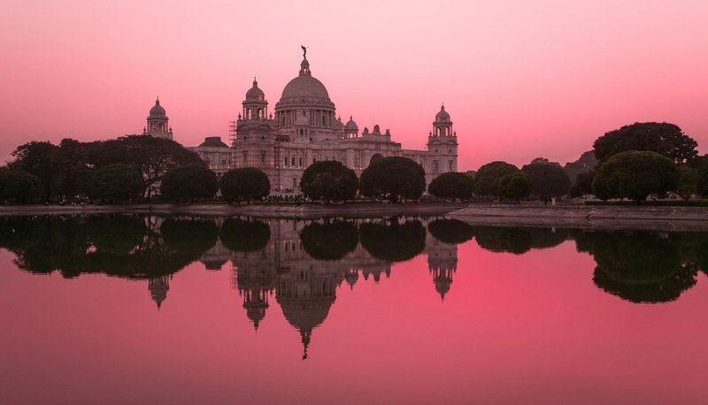The Victoria Memorial reflected in a calm pond under a pink sky in Kolkata