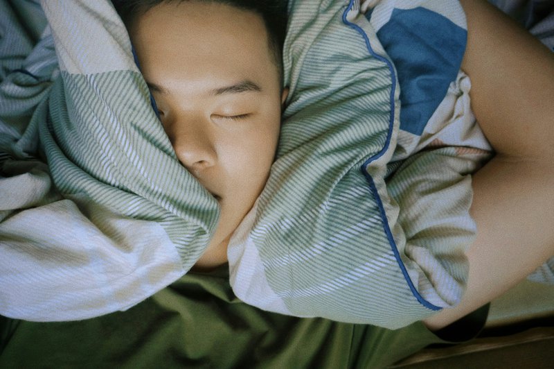 Persoon die in bed slaapt met een kussen tegen de oren.