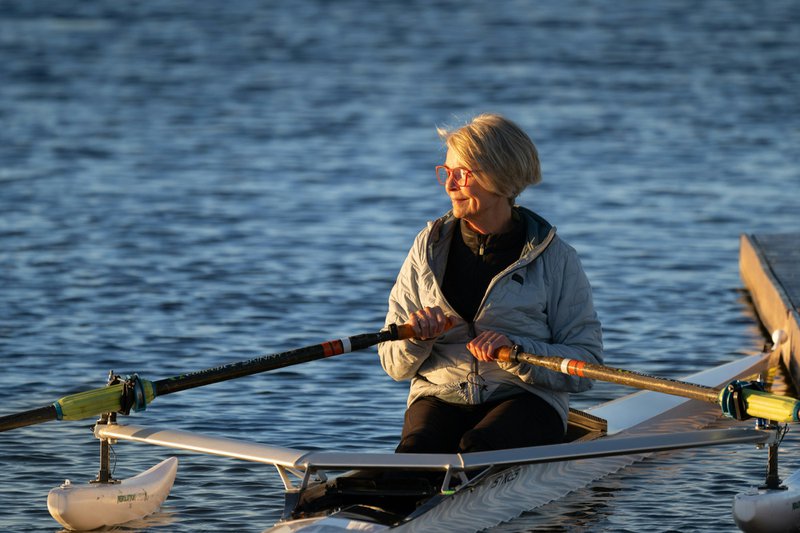 A woman rows her boat on calm water.