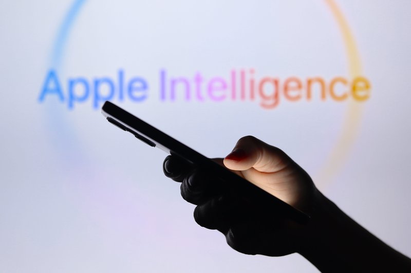 Hand using phone with words 'Apple Intelligence' slightly blurred in the background