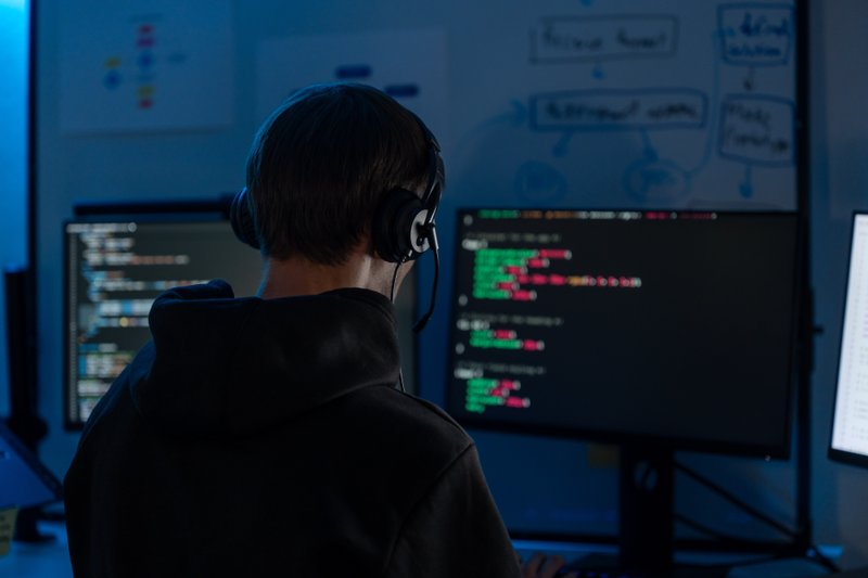 Programming coding at night in a dark room with multiple monitors and a whiteboard.