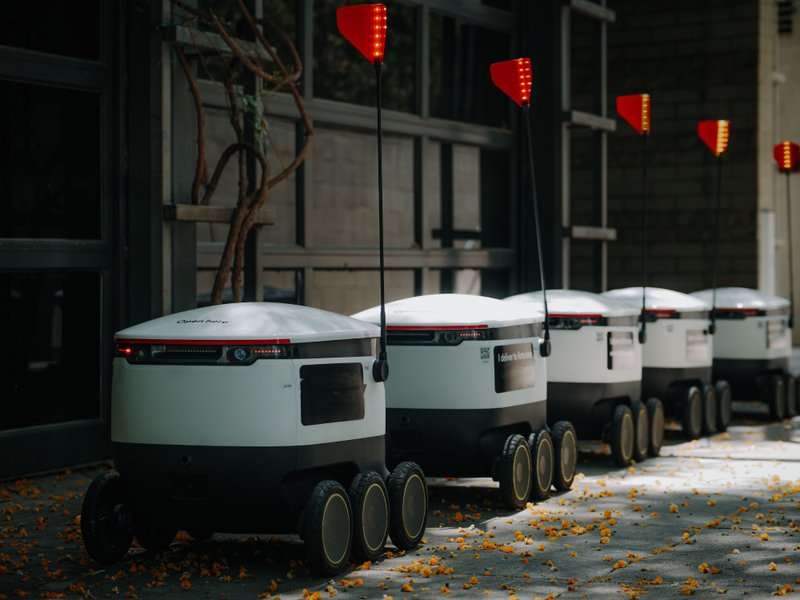 Delivery robots lined up on a city street without a single human delivery driver to be seen.