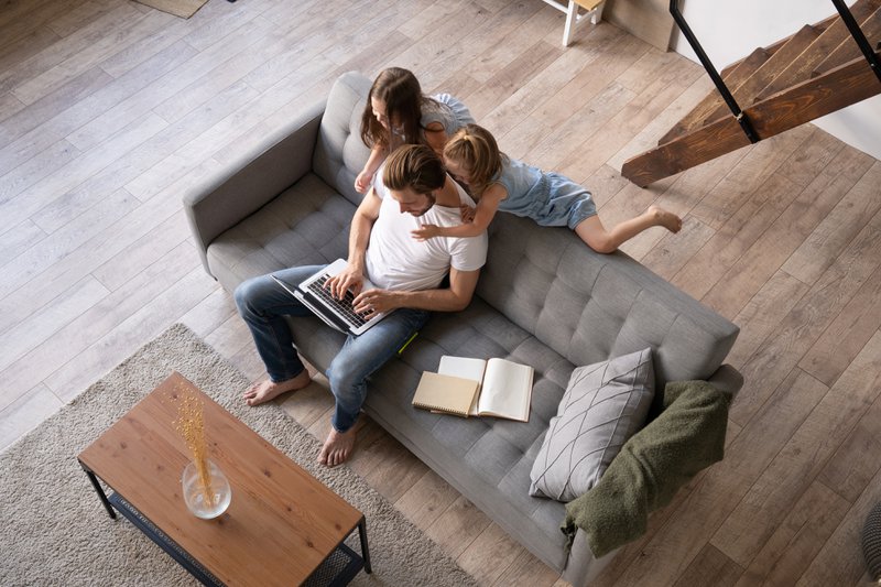 A father with two children on a couch while he is on his laptop.