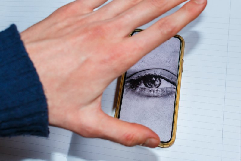 A phone with an eye on the screen, with the user attempting to stop it from listening or watching them.