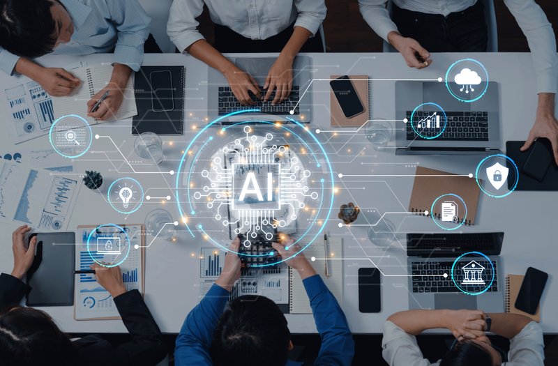 Group gathered around digital devices with a glowing AI symbol highlighting the role of artificial intelligence in modern work.