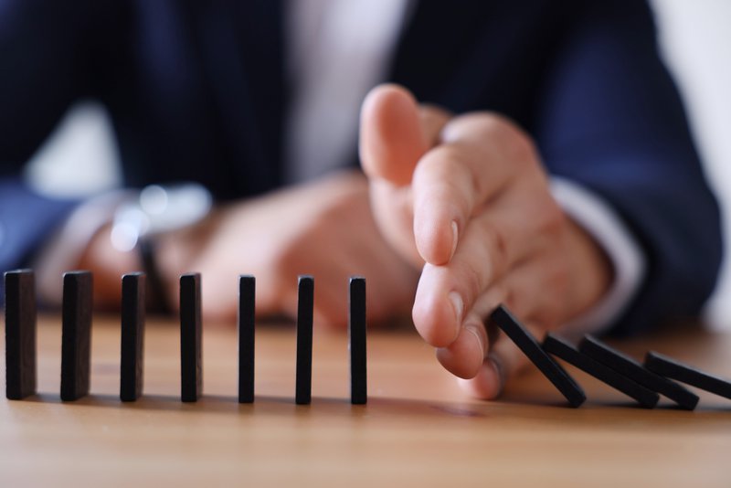 A person's hand stopping the reaction of falling dominoes, illustrating how smaller investments can lessen risk.