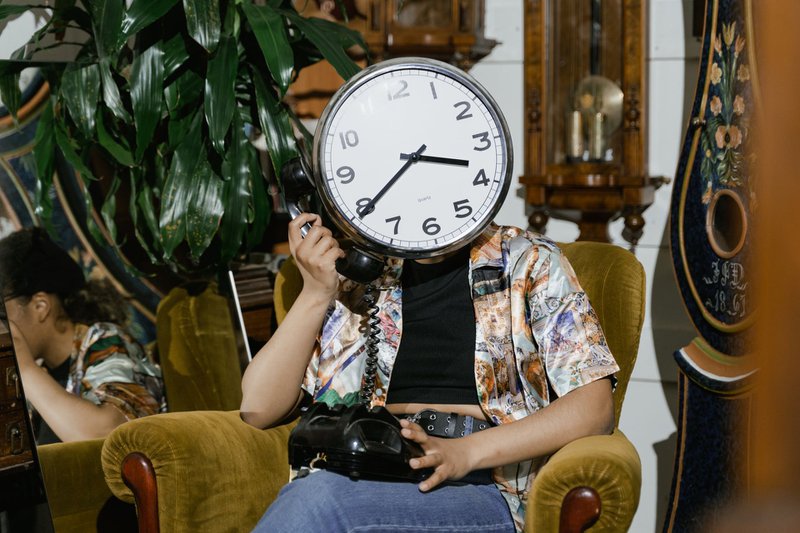 Person with clock face holding vintage telephone in eclectic room setting.