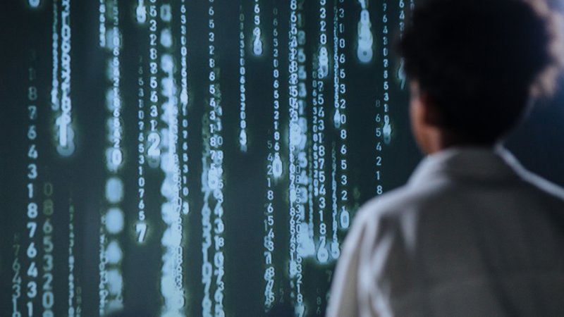 A student standing in front of cascading digital numbers, reflecting on the future of software development in an AI-driven world.