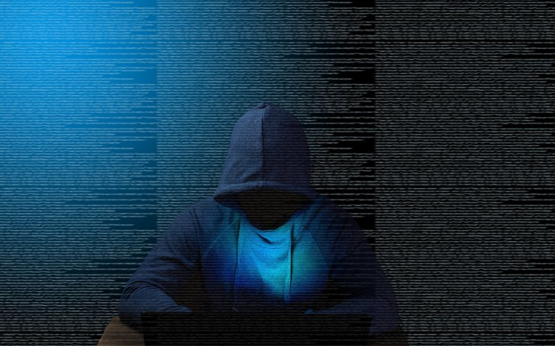 hooded hacker working in silence in front of a backdrop of code