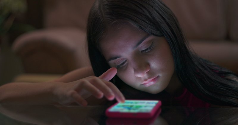 Young person looking at their phone and mindlessly scrolling a night.