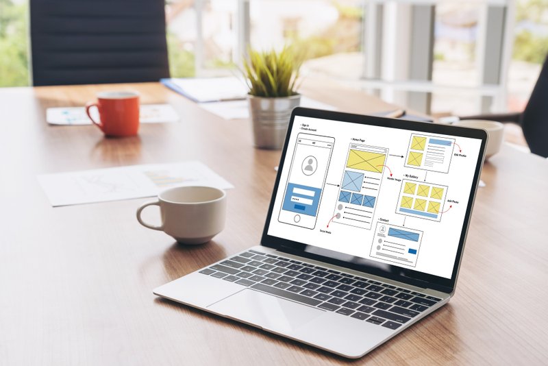 A laptop on a table displaying wireframe mockups of a website or mobile app
