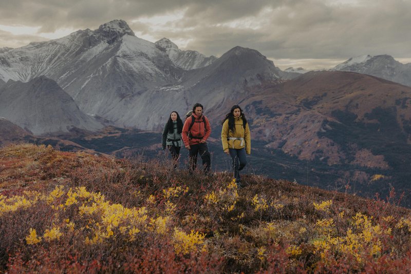 Three friends hiking in shoulder season to Nonda Peak between Toad River and Muncho Lake in the Northern Rockies, with views of the Sentinel mountain range in the background.