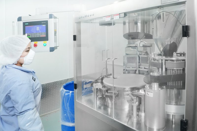 Worker in protective gear inspecting pharmaceutical production line. 