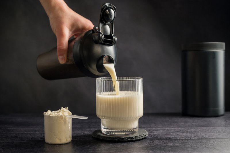 Hand pouring mixed powder supplements into a glass.