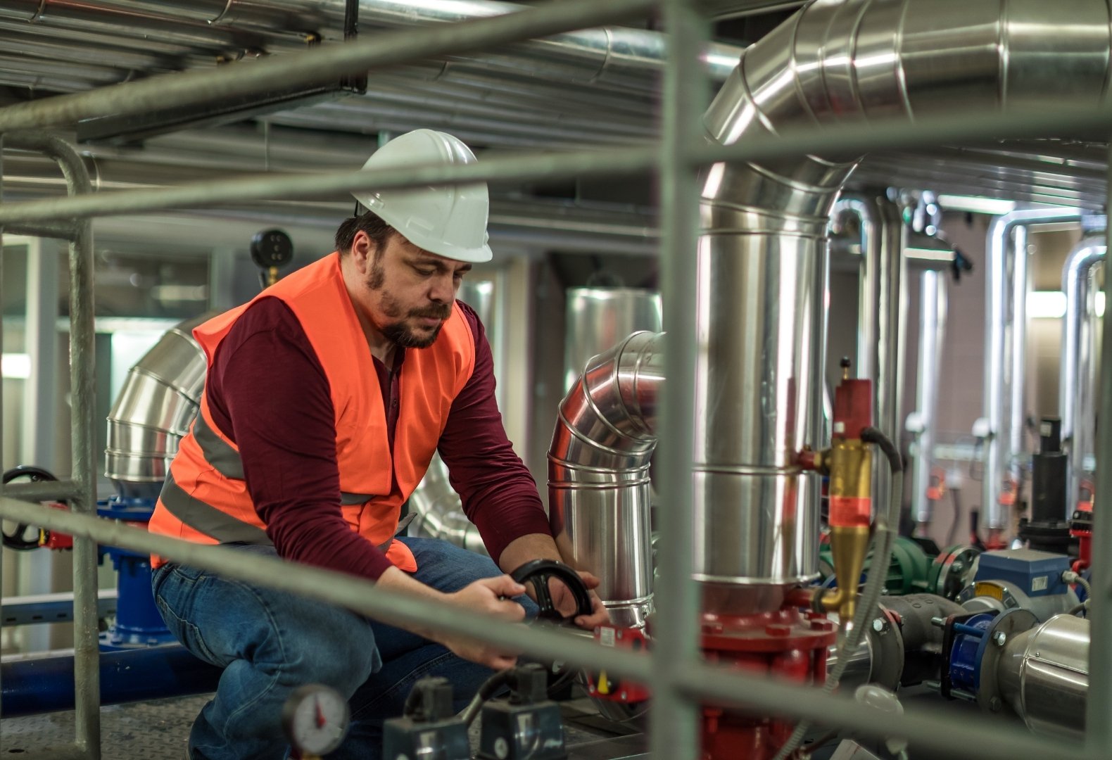 Plumber inspecting the valves and pipes in a boiler room.
