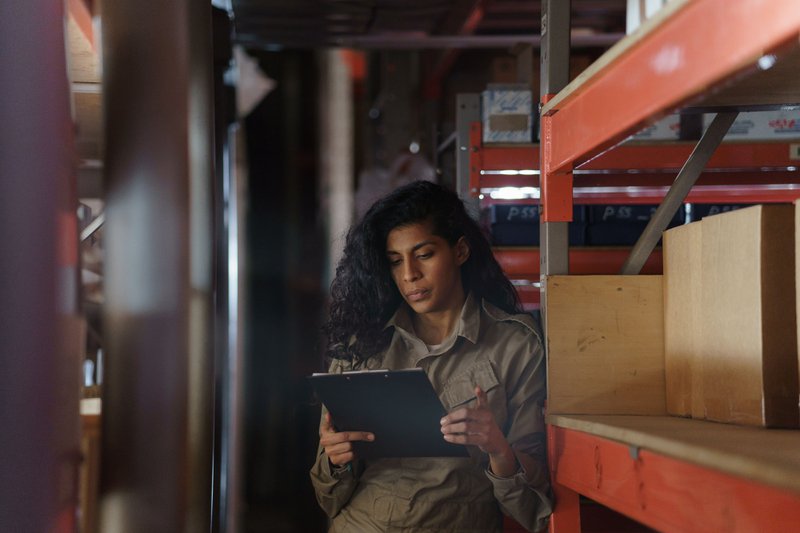Woman in warehouse taking inventory with clipboard, procurement strategy