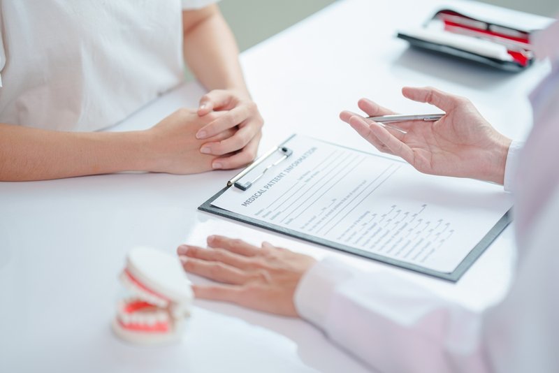 A dentist speaks with a patient in a treatment room, representing real-world clinical practice tied to the cost of dental malpractice insurance.