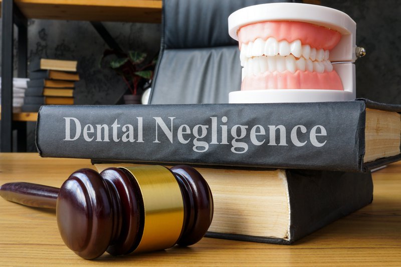 a denture stacked on a book that reads "dental negligence" on the spine
