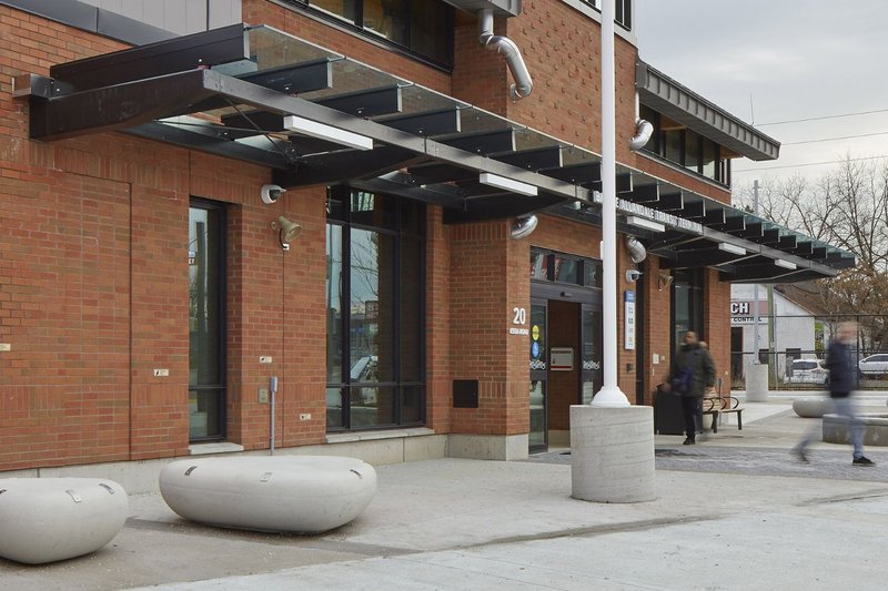 A modern brick building entrance with a clear glass canopy and outdoor benches.
