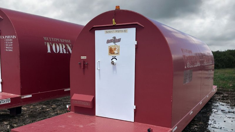 Two Redo Dog mobile shelters with white doors are parked on a muddy outdoor surface.