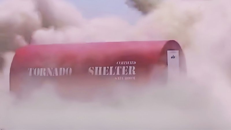 A red mobile shelter enduring a debris impact test in a dust cloud.