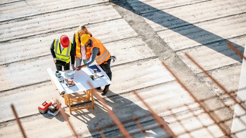 Construction workers reviewing blueprints on-site to plan Remote Workforce Safety Solutions.
