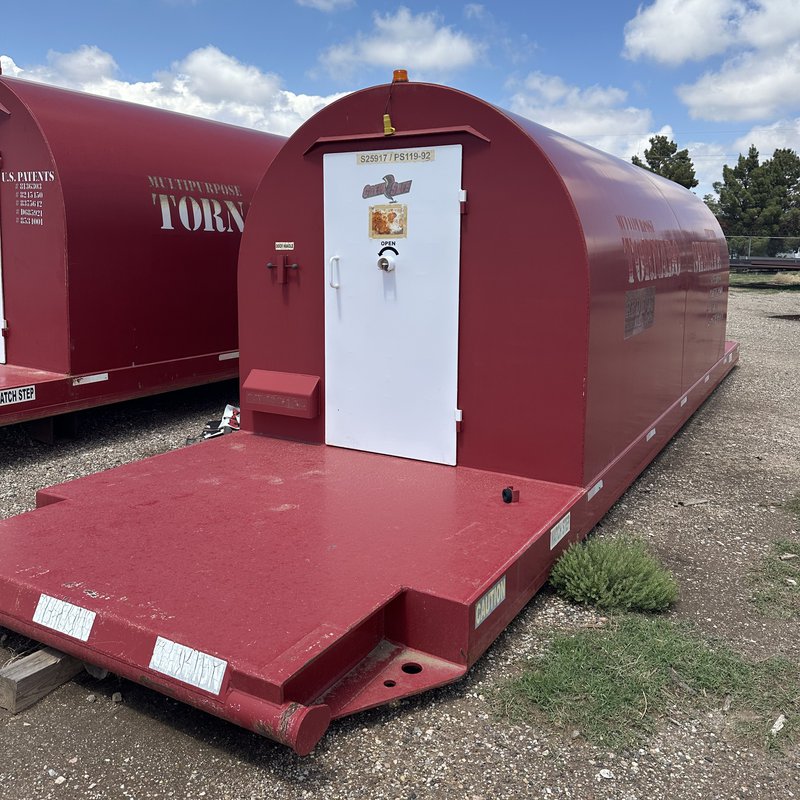 A large, red Red Dog industrial storm shelter sits on a heavy-duty steel skid in a gravel yard.