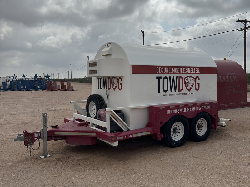 A white and red "TOWDOG" mobile storm shelter by Red Dog Shelters, mounted on a dual-axle trailer for easy transport.