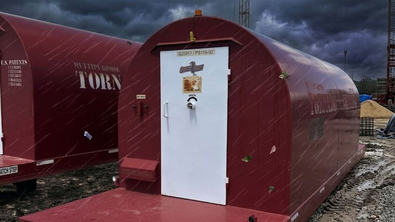 A Red Dog shelter on a muddy construction site, serving as an alternative to in-ground storm shelters.
