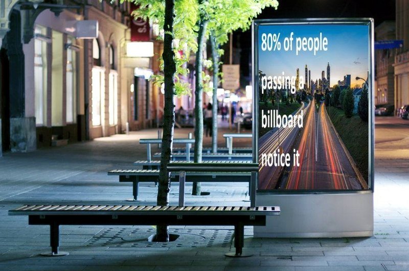 A  small billboard ad displayed beside a bench along a busy commuter foot path