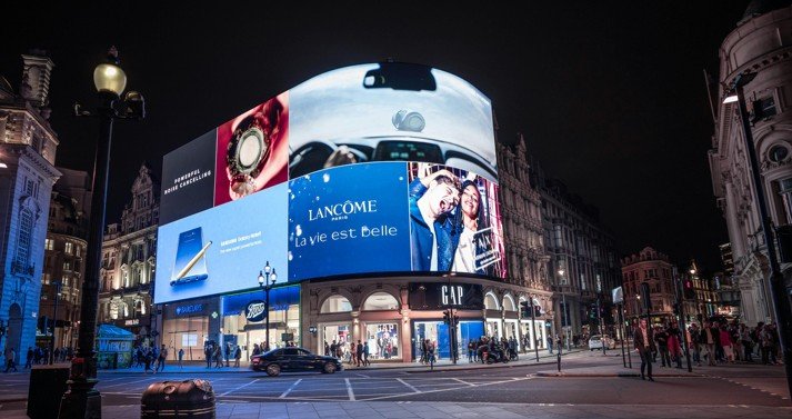 Multiple brand campaigns running on a large digital billboard display in a busy urban corridor at night.