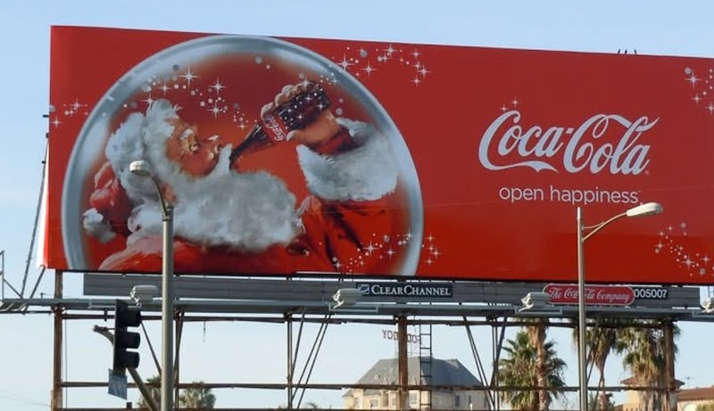 A Coca-Cola holiday billboard with bold red creative and clear brand messaging.