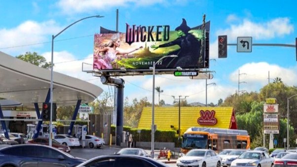 A roadside movie billboard above a busy intersection, illustrating short-term billboard rental for seasonal entertainment advertising
