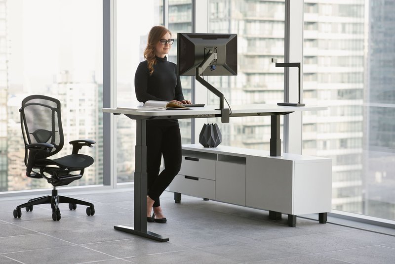 This photo features an employee using ergonomic commercial furniture, specifically an adjustable chair and a standing desk