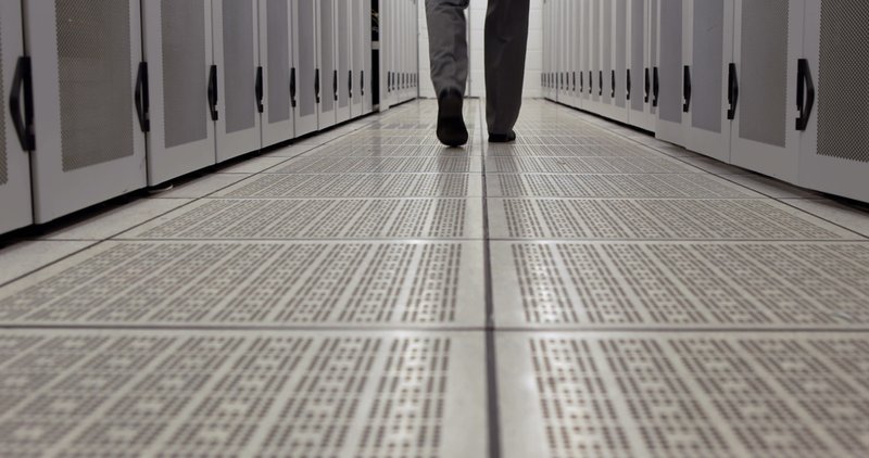 Technician managing cables in a low clearance raised floor system with lifted tiles, highlighting constrained access space and organized subfloor routing in a compact installation.